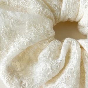 Détail d'un chouchou en coton et lin ivoire avec une broderie florale délicate et dentelle
