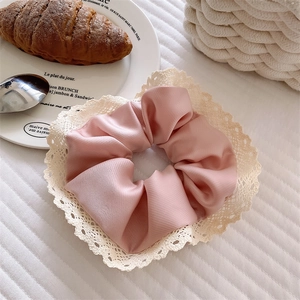 Detail eines rosa Satin-Haargummis mit Vintage-Spitze auf weißer Bettwäsche