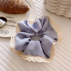 Detail eines fliederfarbenen Satin-Haargummis mit zarter cremefarbener floraler Spitze