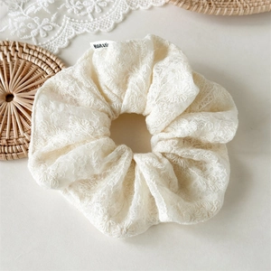 Détail d'un chouchou en dentelle crème avec broderie florale et étiquette tissée