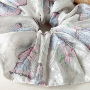 Détail d'un chouchou en satin avec imprimés papillons roses et bleus et paillettes