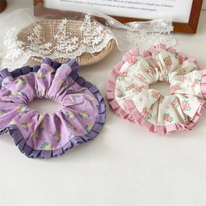 Detail von lila und cremefarbenen Blumen-Scrunchies mit Rüschenrand auf Spitze