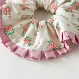 Detailansicht eines cremefarbenen Haargummis mit Blumenmuster und rosa Rüschen