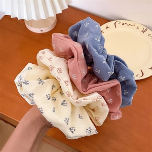 Détail de trois chouchous à motifs floraux en bleu, rose et beige avec bordure en dentelle