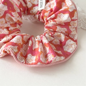 Détail macro du chouchou floral en tissu avec bords roses et étiquette de marque