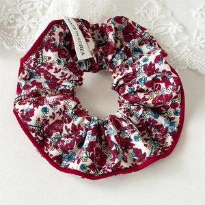 Détail d'un chouchou floral avec bords rouges et étiquette Made in Korea sur dentelle