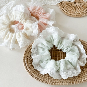 Detail of three embroidered lace scrunchies in cream, light pink and green colors