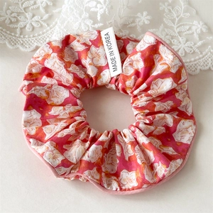 Détail du chouchou floral avec motifs de fleurs roses et orange sur tissu texturé