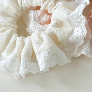 Close-up of floral embroidery and lace trim on soft cream and pink scrunchies