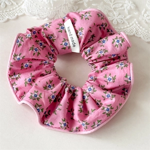 Détail macro du chouchou floral en tissu rose avec étiquette fait main sur dentelle