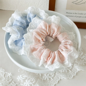 Close-up of floral lace scrunchies in pastel blue and pink on a white ceramic plate