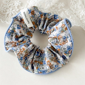 Détail d'un chouchou floral avec liseré bleu et étiquette hand made sur de la dentelle