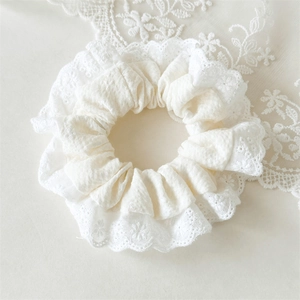 Close-up of white floral lace scrunchie with intricate embroidery and ruffled texture