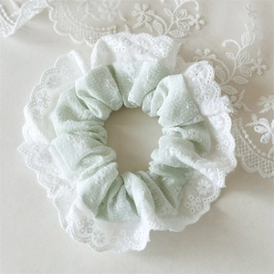 Detailed close-up of light green floral lace hair tie with intricate white embroidery
