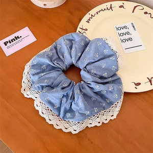 Détail d'un chouchou bleu fleuri avec bordure en dentelle blanche sur bois