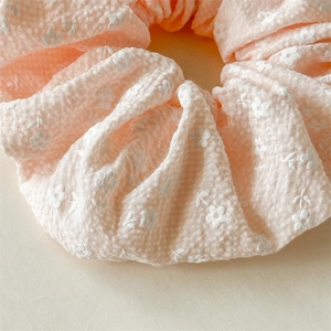 Detail von rosa Seersucker-Haargummi mit weißem Blumenmuster und weicher Plissee-Textur