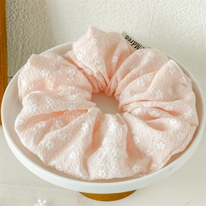 Nahaufnahme von rosa Scrunchie mit Blumenstickerei und Markenetikett auf Tablett