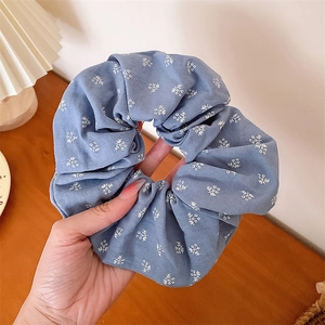 Gros plan d'un chouchou bleu à fleurs avec bords en dentelle tenu délicatement à la main