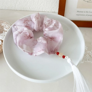 Close-up of pink floral scrunchie with white silk tassel and beads on a ceramic plate