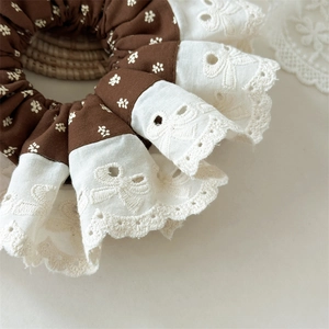 Macro shot of brown floral fabric and white lace scrunchie with bow embroidery