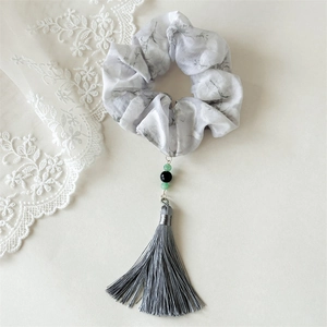 Detailed view of ink floral scrunchie with tassel and green bead charms on white lace background