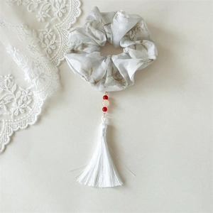 Close-up of ink style scrunchie with floral pattern, red beads and long white tassel