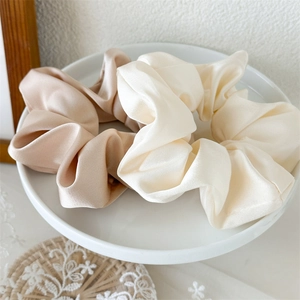 Dettaglio di eleganti elastici scrunchies in raso champagne e crema su un piatto bianco