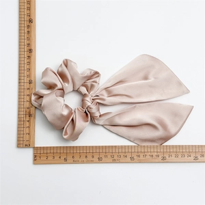 Dettaglio dello scrunchie in raso rosa con fiocco che mostra il tessuto e le misure
