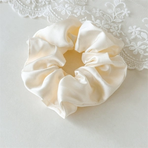 Dettaglio dell'elegante elastico scrunchie in raso avorio con trama in seta morbida