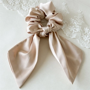Tessitura dettagliata di uno scrunchie in raso champagne con nastro a fiocco lungo