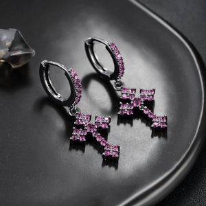 Detail van zwarte kruisoorbellen met roze zirkonia micro-pave op een mat zwarte schotel