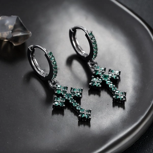 Detail van zwarte oorbel met kruishanger en groene zirkonia voor een moderne look