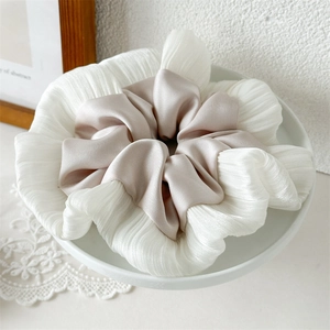 Dettaglio dell'elastico scrunchie in organza bianca e raso champagne su piatto ceramico