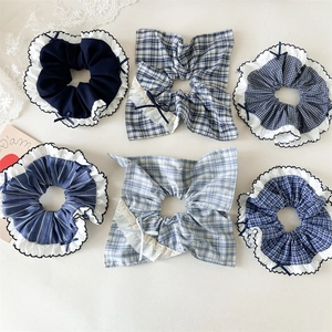 Flat lay of six blue plaid and lace scrunchies with bow details on a soft fabric base