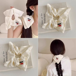 Detail of cream lace hair scrunchie with red cherry embroidery and heart-shaped fabric patch