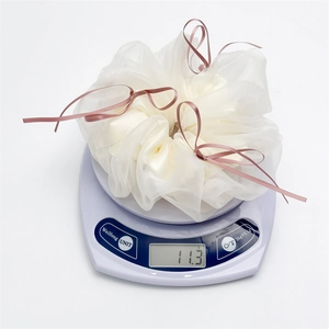 Vue détaillée d'un chouchou en organza crème avec nœuds roses pesant 11,3g sur une balance