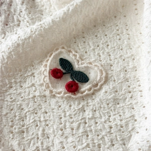 Close-up of white lace triangle headband featuring embroidered red cherry and heart detail