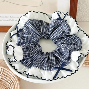 Detail of blue gingham scrunchie with white ruffled edges and small navy ribbon bows
