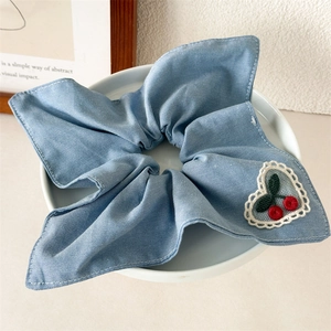 Detail of denim blue hair scrunchie with heart cherry embroidery in a ceramic bowl