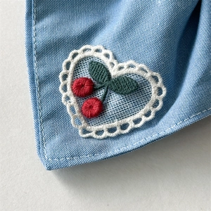 Close-up of denim blue hair tie featuring heart lace embroidery and red cherry pattern