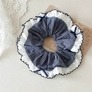 Detailed close-up of blue gingham scrunchie with white wavy trim and satin bow