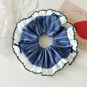 Close-up of blue striped scrunchie with white wavy lace trim and small navy bows