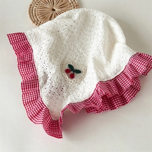Detail of white lace baby hat featuring red checkered ruffle and cherry embroidery