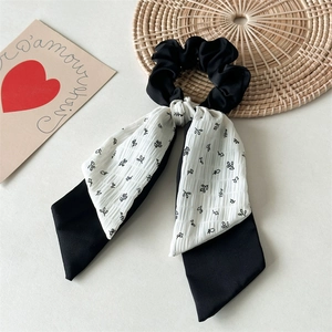 Detailed view of black floral scrunchie with layered ribbon streamers on textured tray