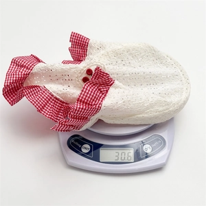 Detailed view of white eyelet lace headscarf with cherry red gingham ruffles weighing 30.6g