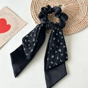 Detail view of a black floral scrunchie with long ribbons and satin texture on a mat
