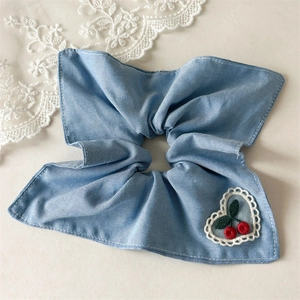 Détail d'un chouchou bleu clair avec patch en dentelle cœur et broderie cerise