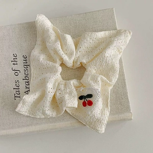 Detailed macro of cream cotton scrunchie with lace heart and cherry embroidery