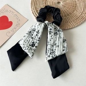 Close-up of black floral scrunchie with long ribbon streamers on artistic props