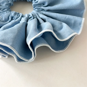 Detail of light blue denim scrunchie showing fine chambray texture and white overlock stitching